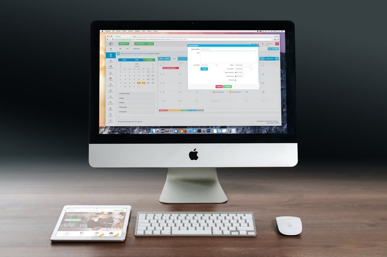 A sleek office setup featuring an Apple iMac, iPad, and keyboard on a wooden desk.